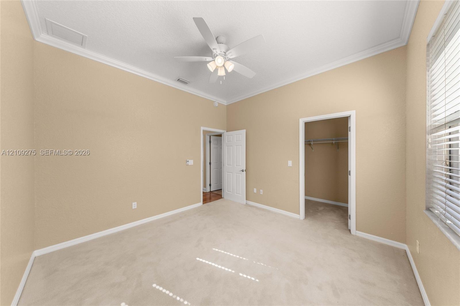 Interior space featuring high ceilings with crown molding, neutral carpeting, a ceiling fan with integrated lighting, and a built-in reach-in closet