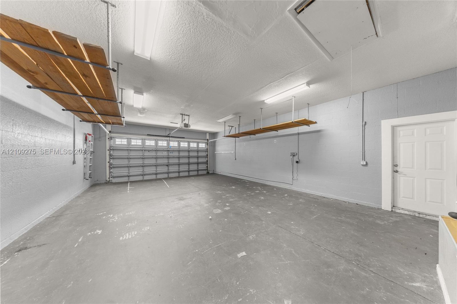 Multi-car garage featuring overhead storage shelving, fluorescent lighting, concrete flooring, and an exterior access door
