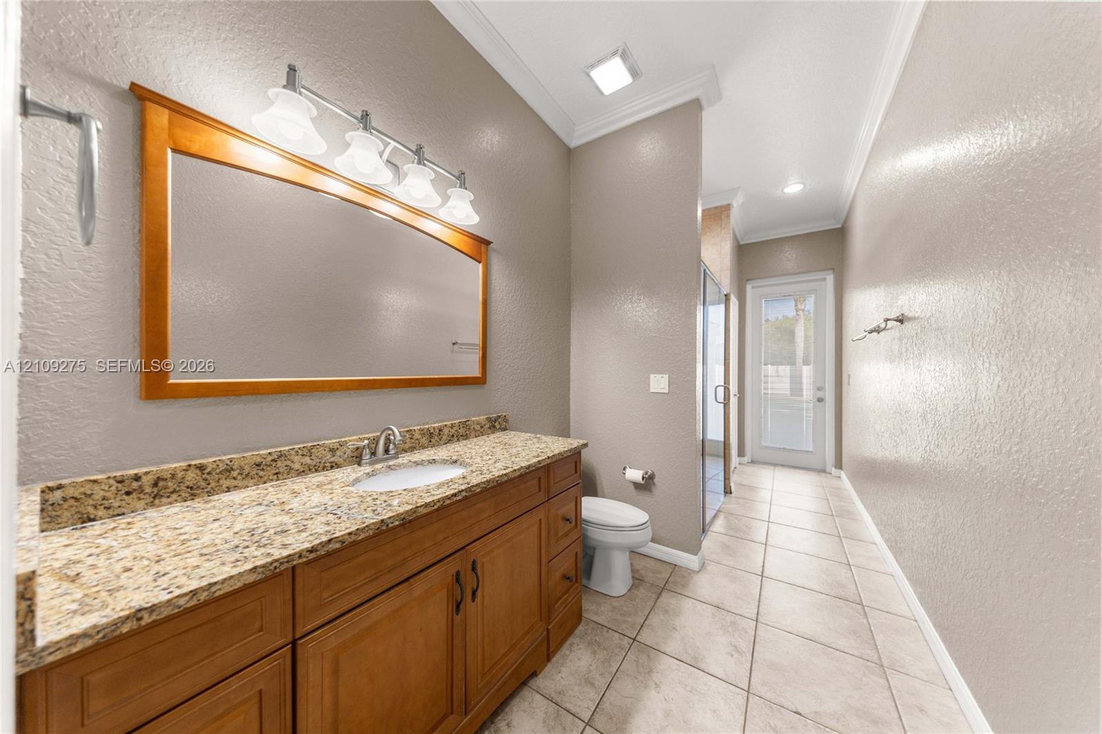 Bathroom featuring a wood-finish vanity with stone countertop, an undermount sink, a framed wall mirror, and large-format tile flooring