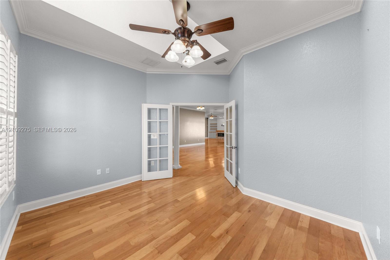 Room featuring wood-finish flooring, tray ceiling, ceiling fan with integrated lighting, and French doors with glass panes
