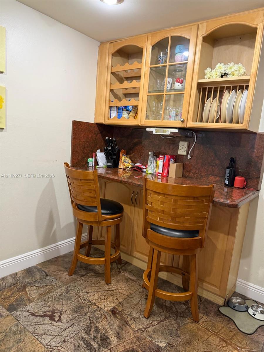 Custom built-in cabinetry featuring glass-paneled display doors, integrated wine rack, and open plate shelving with stone-finish countertops and backsplash