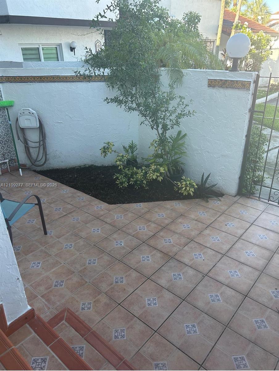 Enclosed courtyard featuring patterned ceramic tile flooring, a structured garden bed, white masonry perimeter walls, and iron gate access