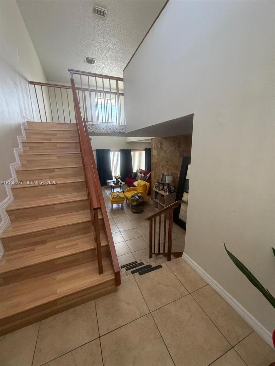 Staircase with wood-finish treads, metal railing, ceramic tile flooring, and stone-surround accent wall
