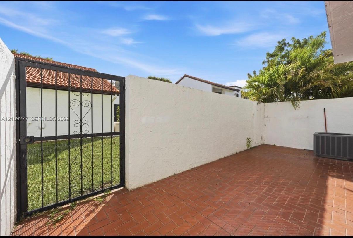 Enclosed outdoor patio featuring herringbone-patterned tile flooring, stucco privacy walls, and a decorative wrought-iron gate
