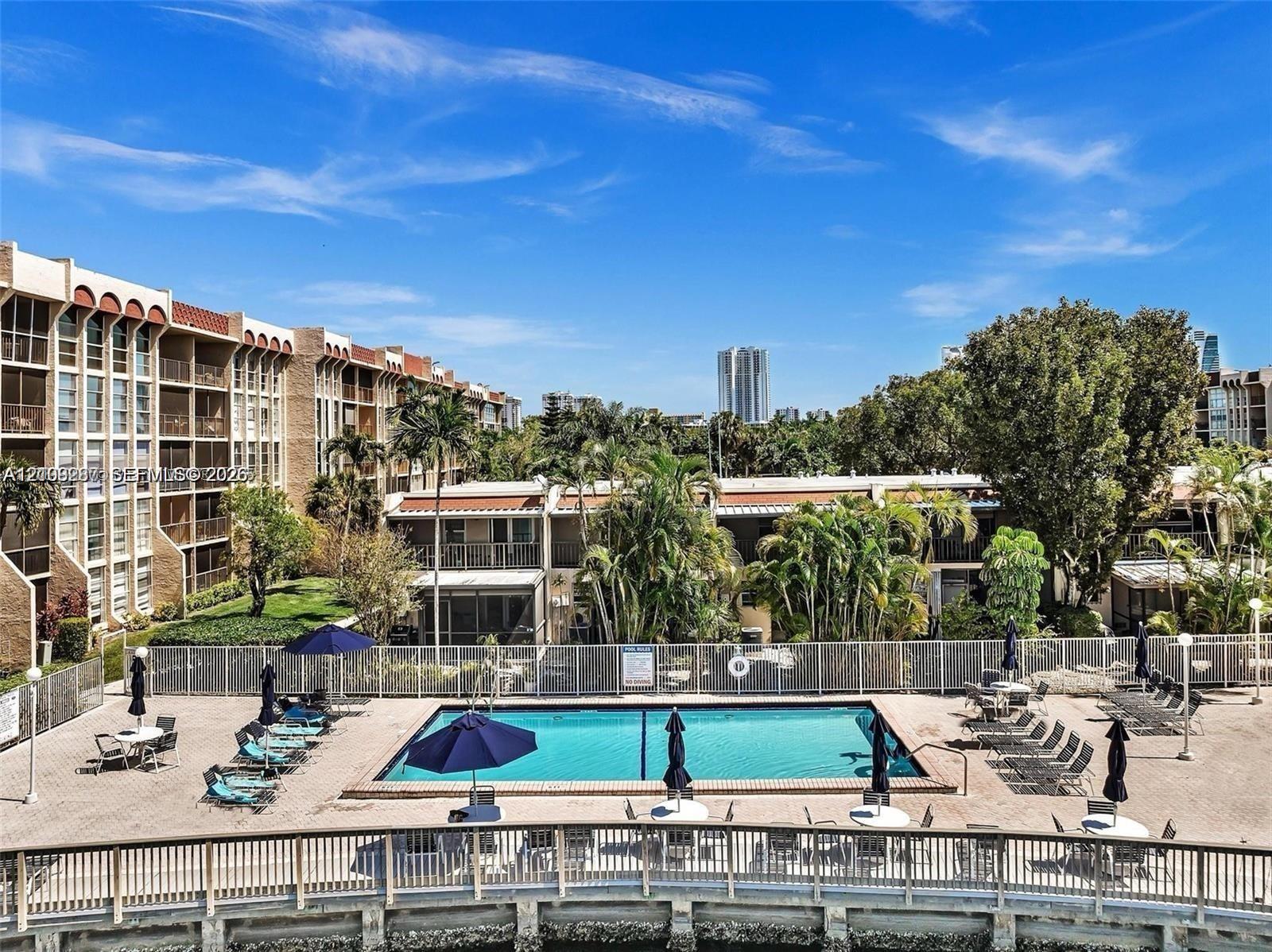 Rectangular swimming pool featuring a brick-paver deck, perimeter safety fencing, and a surrounding multi-level residential complex