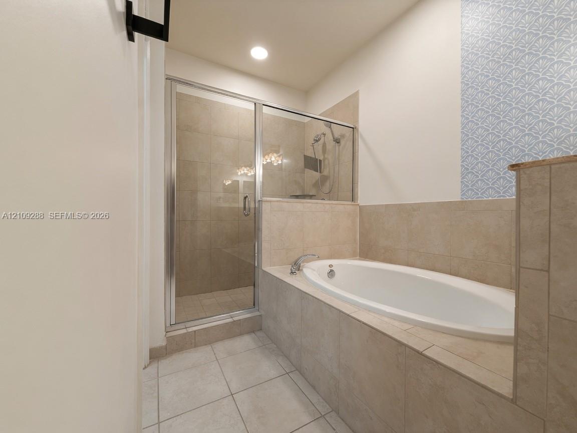 Built-in oval soaking tub with tile surround, glass-enclosed shower with tiled interior, and decorative patterned tile wall accent