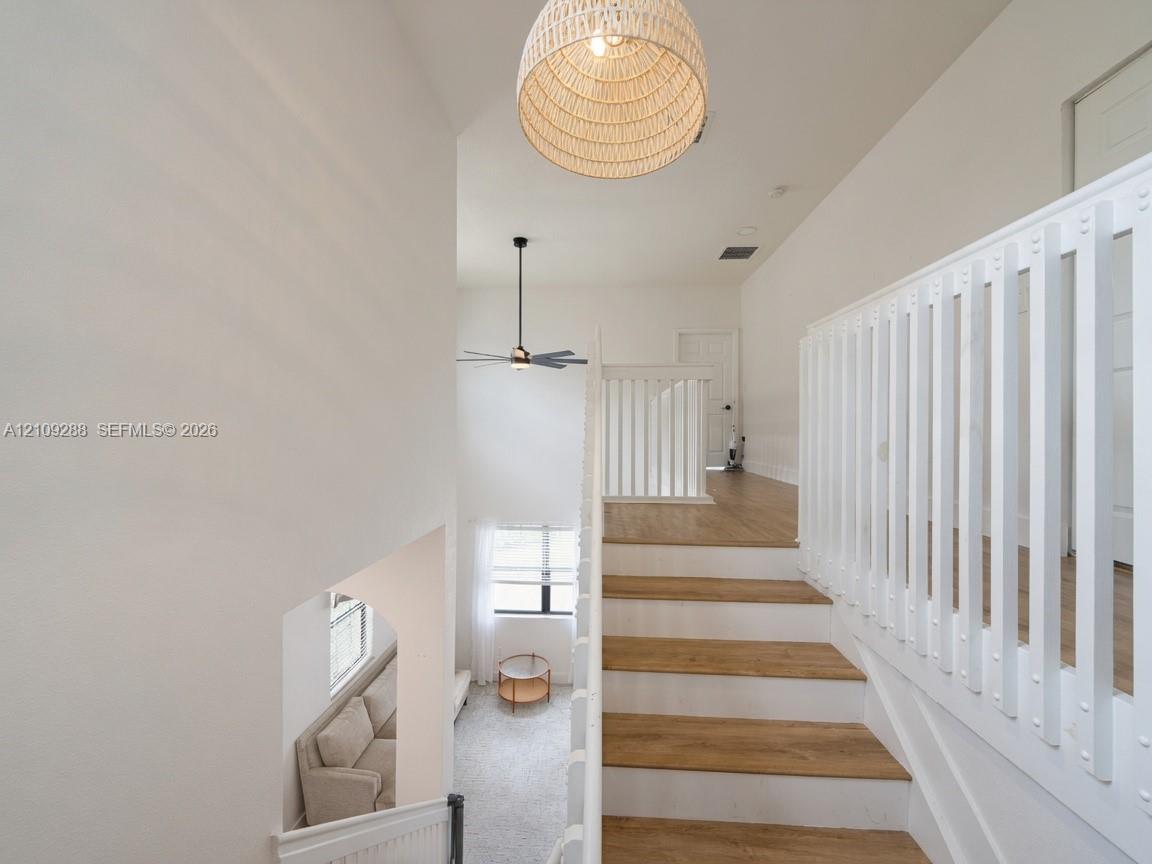 Staircase featuring wood-finish treads and white risers, enclosed by a white vertical-slat balustrade with a prominent woven pendant light fixture