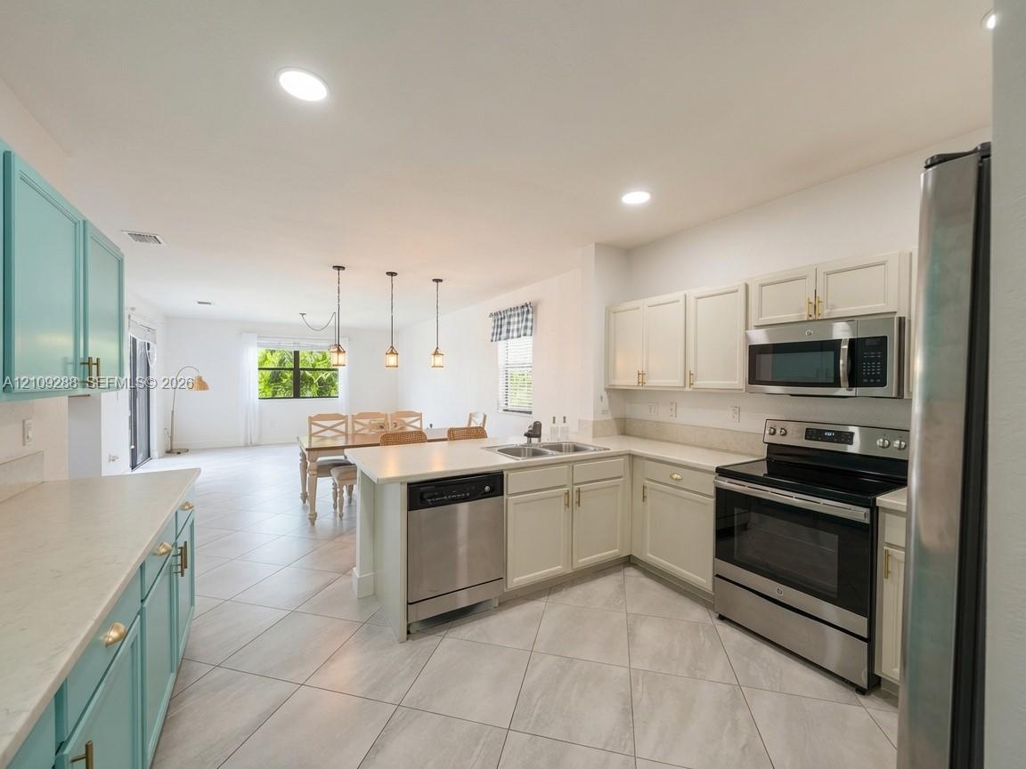 Kitchen featuring light-toned cabinetry, stainless steel appliances, a center island with a built-in dishwasher, neutral countertops, and tile flooring