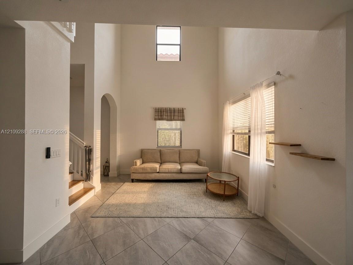 Interior featuring expansive vaulted ceilings, neutral wall tones, large-format tile flooring, a prominent arched architectural detail, and custom wall-mounted shelving