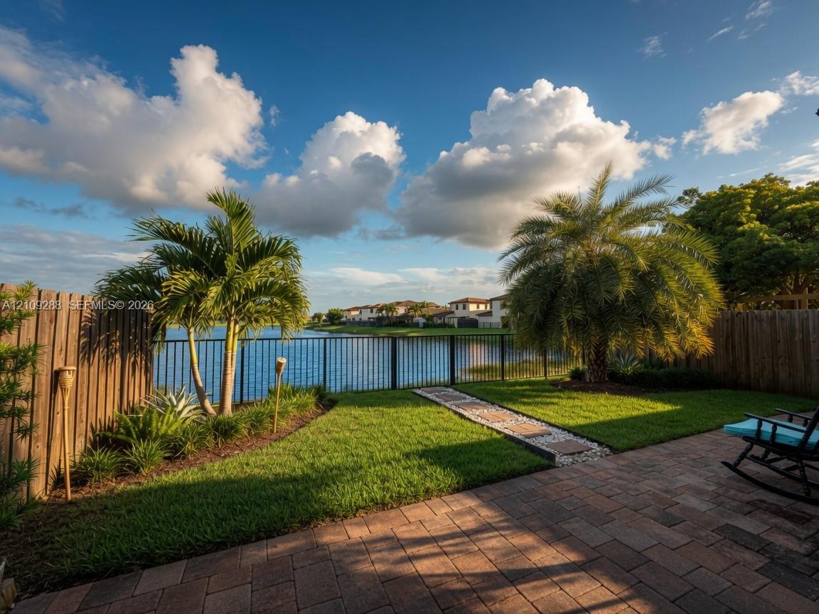 Waterfront backyard featuring a paver patio, a grass lawn, decorative stone walkway, and perimeter fencing