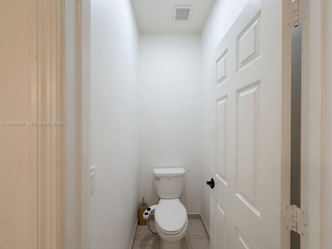 Enclosed space featuring a six-panel door with matte black hardware, tile flooring, and a porcelain toilet with an integrated bidet attachment