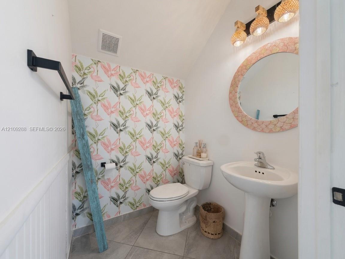 Pedestal sink with polished chrome faucet, patterned wallcovering, tile flooring, and multi-light vanity fixture