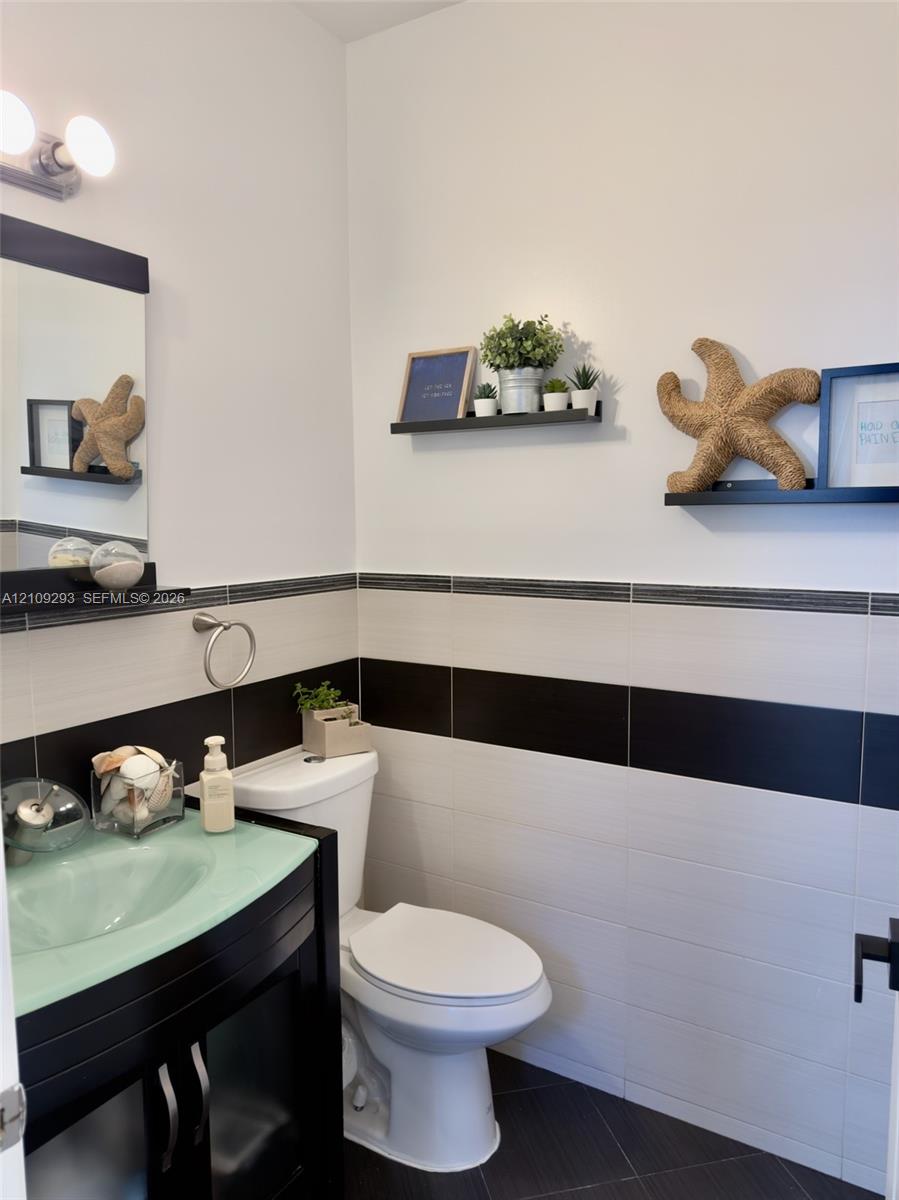 Vanity featuring a green glass vessel sink and dark finish cabinetry, complemented by wall-mounted shelving and dual-tone horizontal tile wainscoting