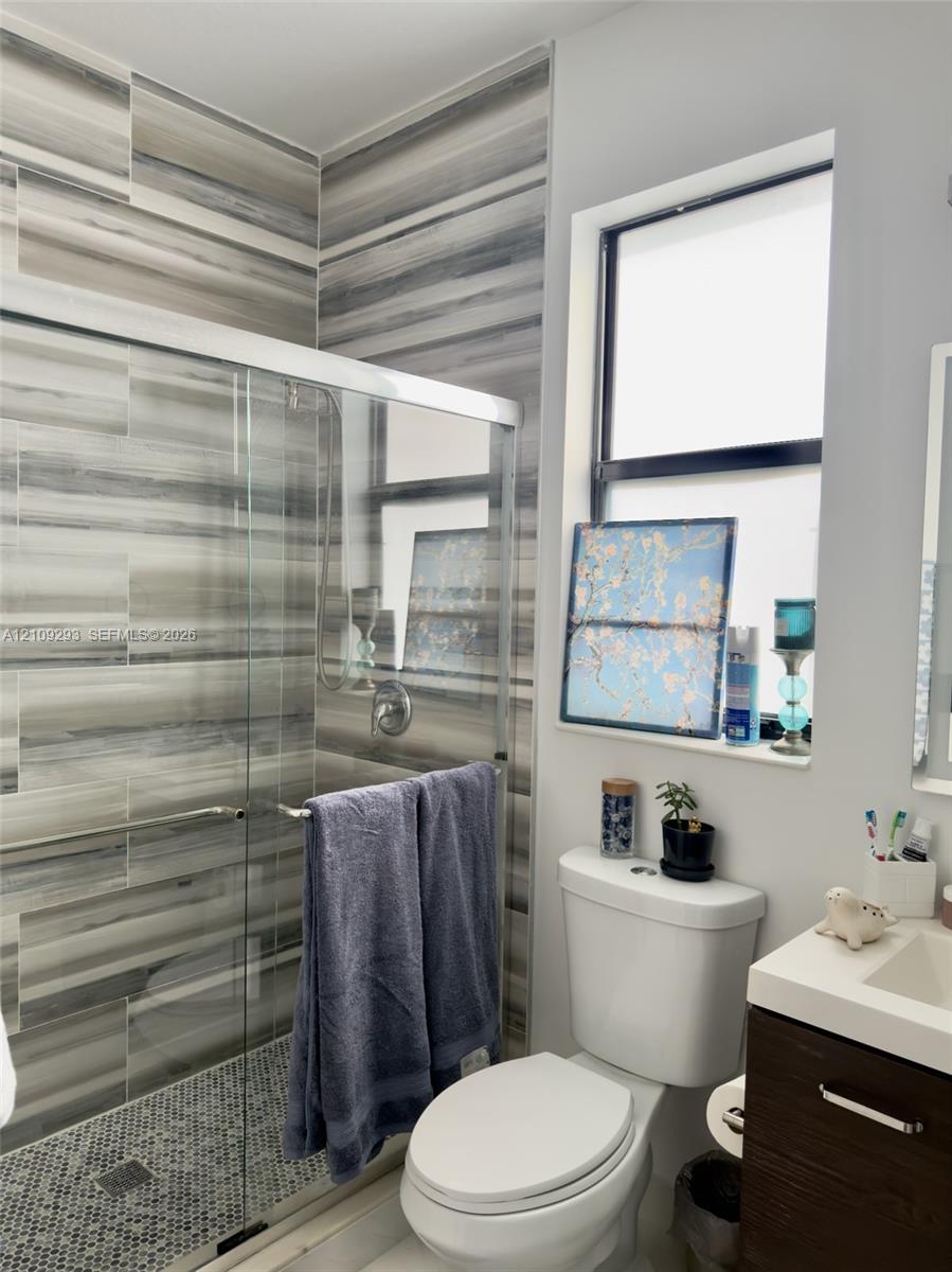 Walk-in shower featuring floor-to-ceiling striated tile, mosaic-tiled shower floor, glass enclosure, and a wood-finish vanity with a rectangular sink and solid surface countertop