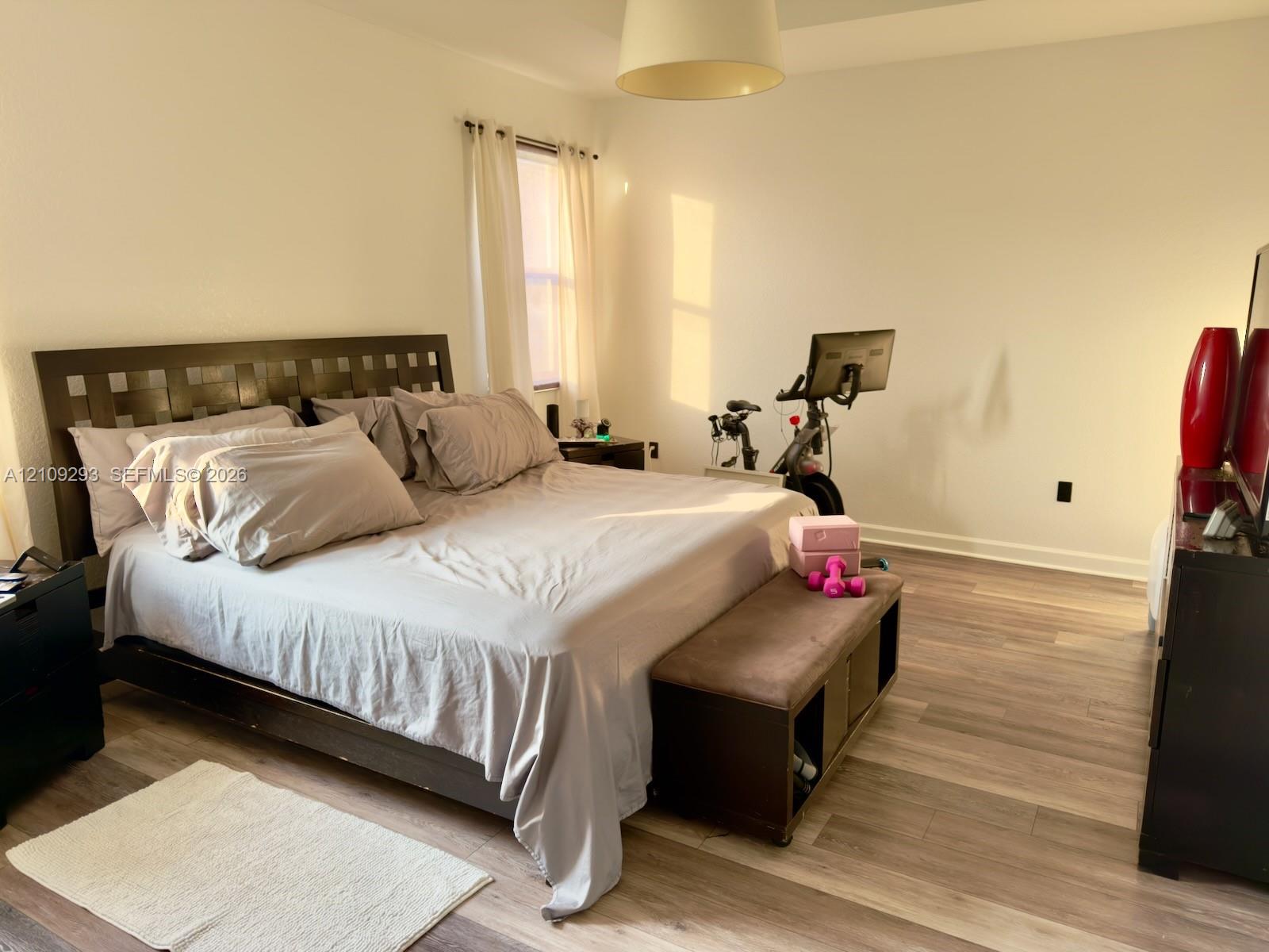 Room featuring wood-finish flooring, a recessed tray ceiling, and a central pendant light fixture