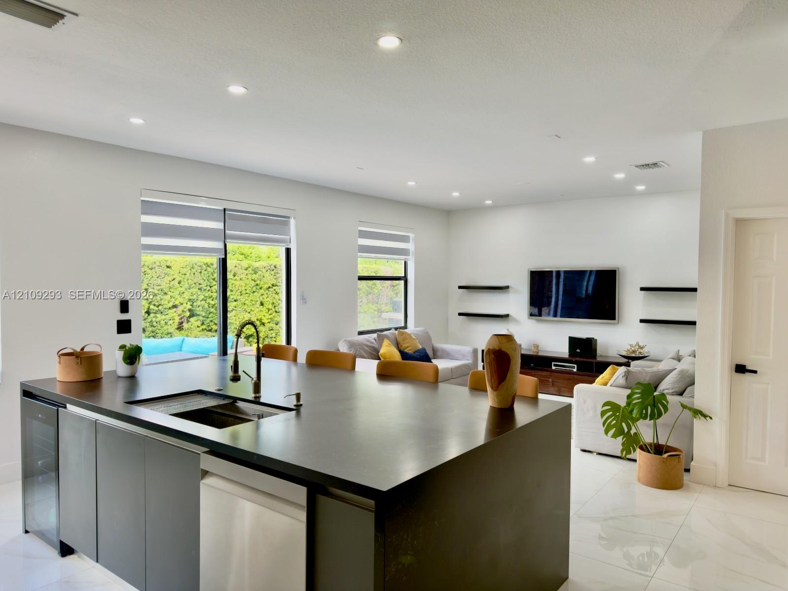 Kitchen island featuring a stone countertop, under-mount sink with a pull-down faucet, integrated wine refrigerator, and light-colored tile flooring