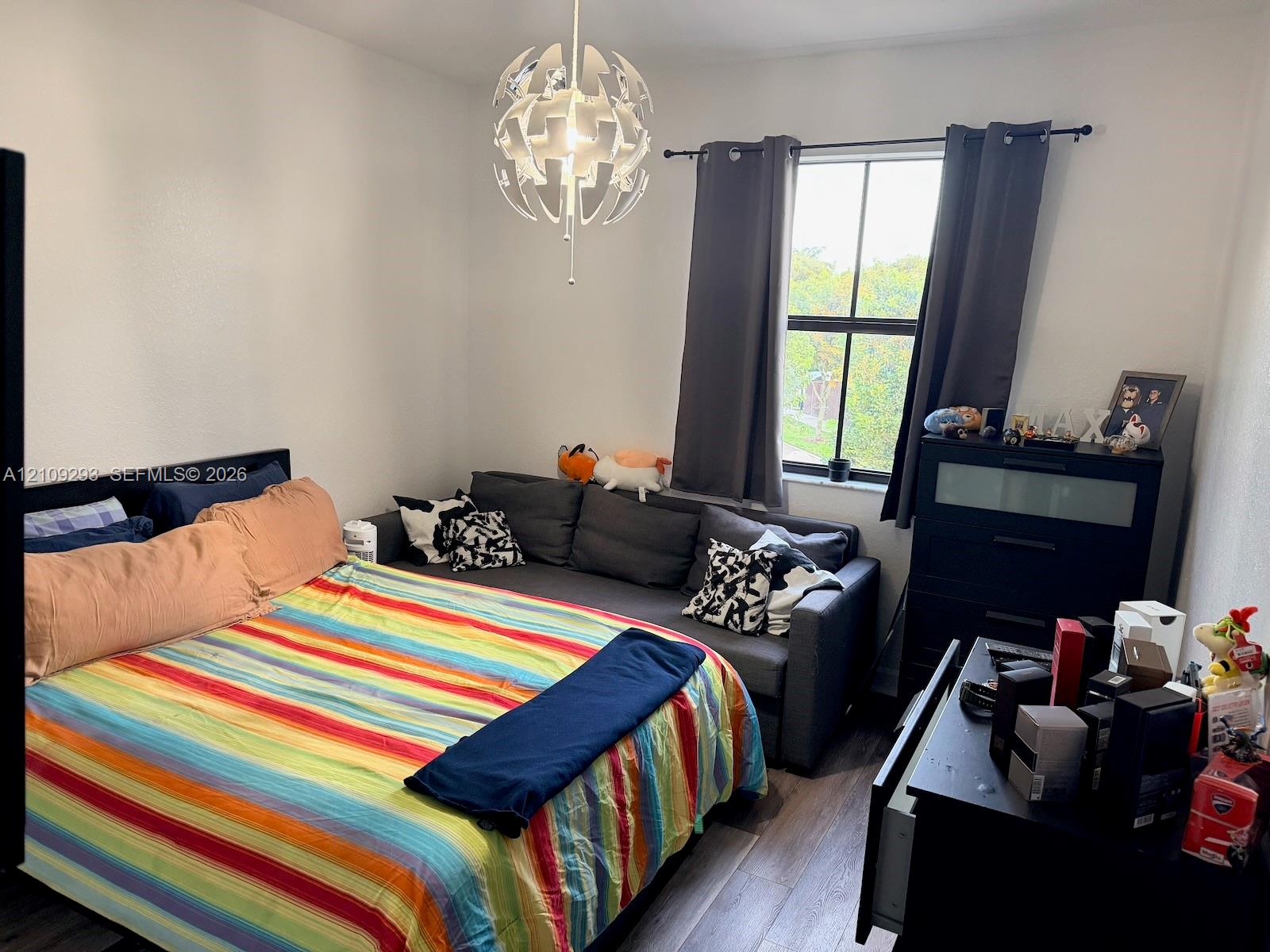 Bedroom featuring wood-finish flooring, a multi-pane window with a black frame, and a decorative modern spherical chandelier