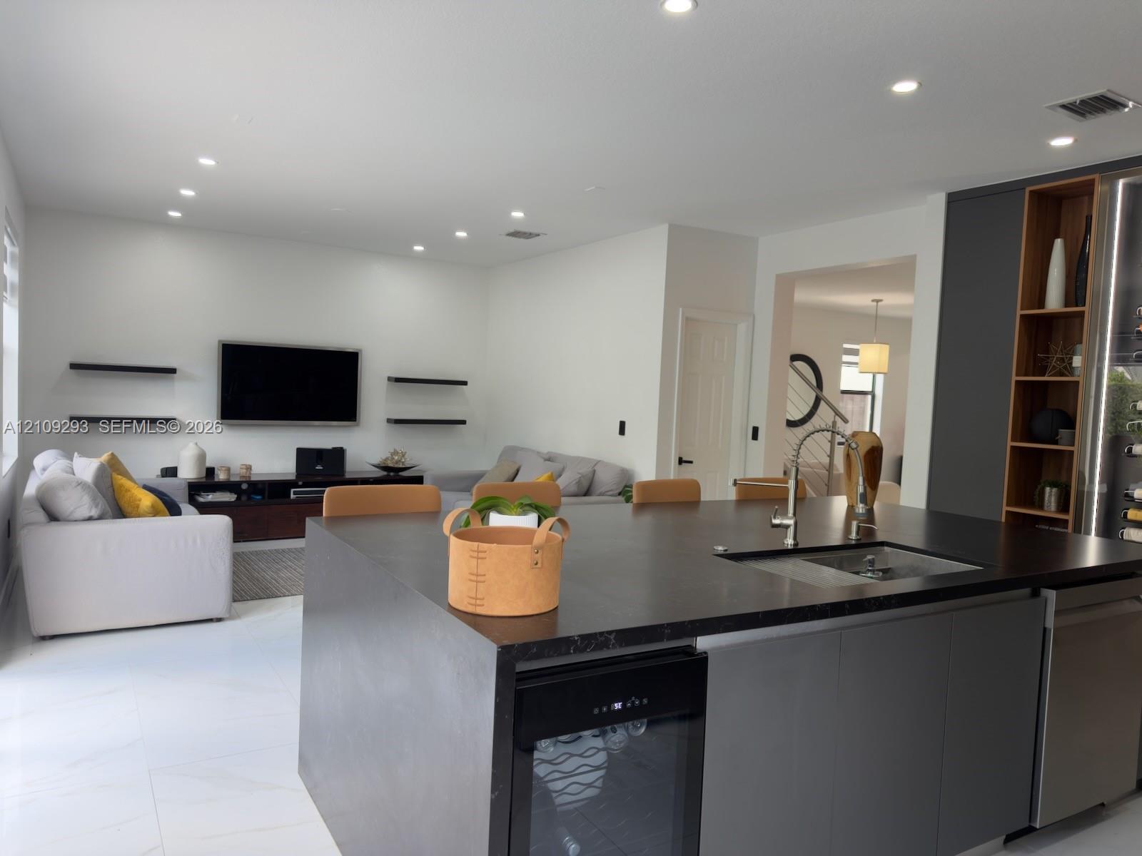 Large kitchen island featuring a dark stone countertop, undermount sink, integrated wine cooler, and flat-panel cabinetry