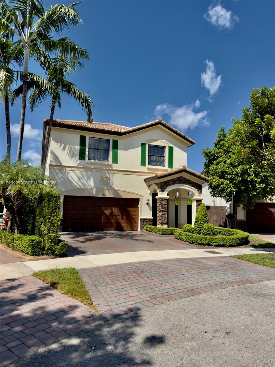 Two-story stucco exterior with a tiled roof, stone-veneer entry columns, a multi-car garage, and a paver driveway