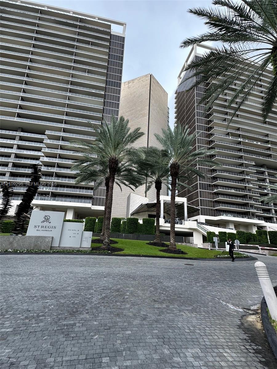 High-rise architectural exterior featuring glass-railed private balconies, paved motor court, mature palm trees, and manicured landscaping