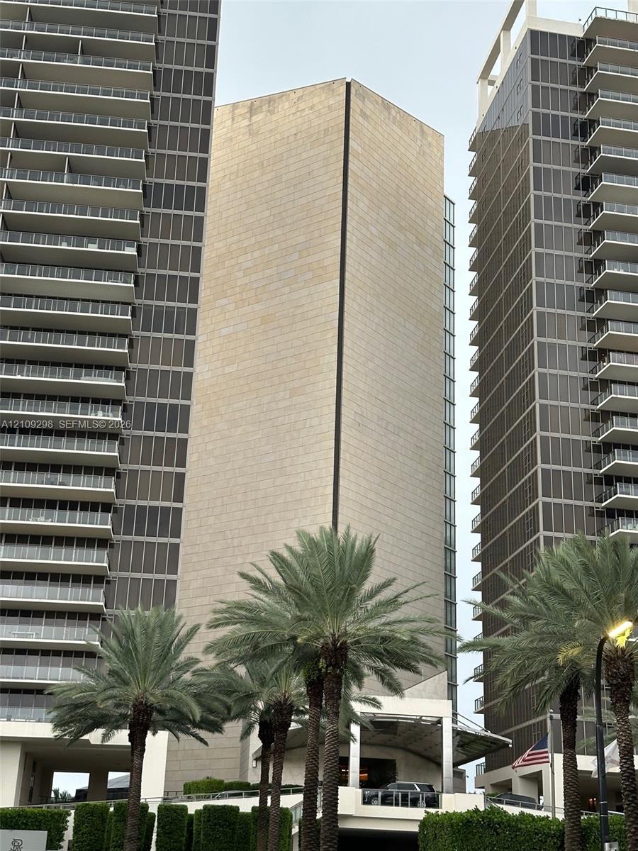 High-rise architectural exterior featuring stone cladding, multi-story glass curtain walls, and stacked private balconies, complemented by mature palm landscaping
