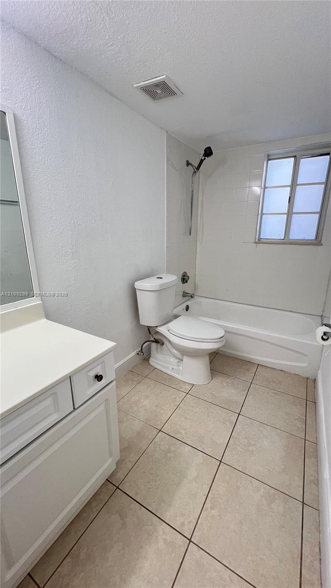 Bathroom featuring square tile flooring, a white vanity cabinet with a solid surface countertop, and a tub-shower combination with full-height wall tile