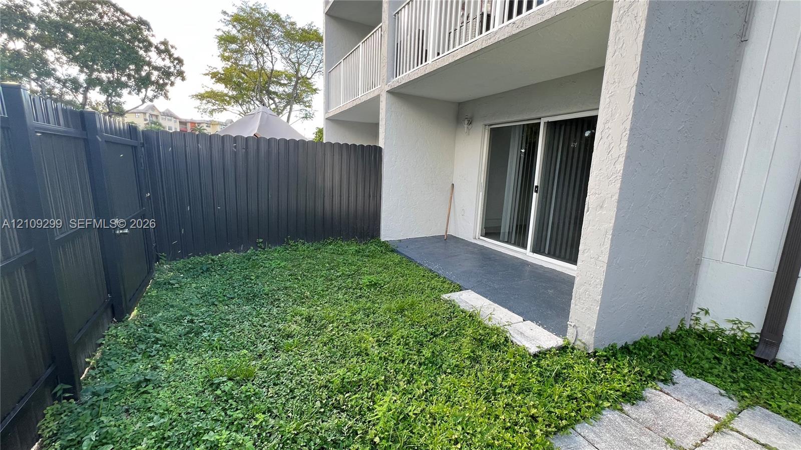 Private fenced-in outdoor space featuring a concrete patio, grassy yard area, and a sliding glass door entry