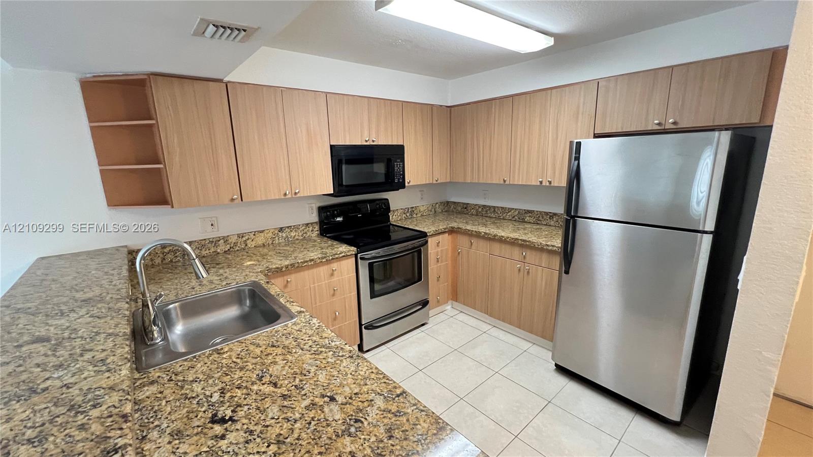 Kitchen featuring light-finish cabinetry, stone-surface countertops, stainless steel appliances, ceramic tile flooring, and a single-basin undermount sink with a high-arch faucet