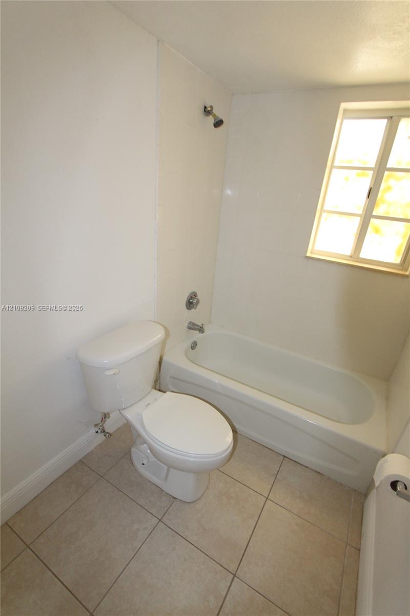 Bathroom featuring ceramic tile flooring, white porcelain tub and shower combination, polished metal fixtures, and a dual-pane window