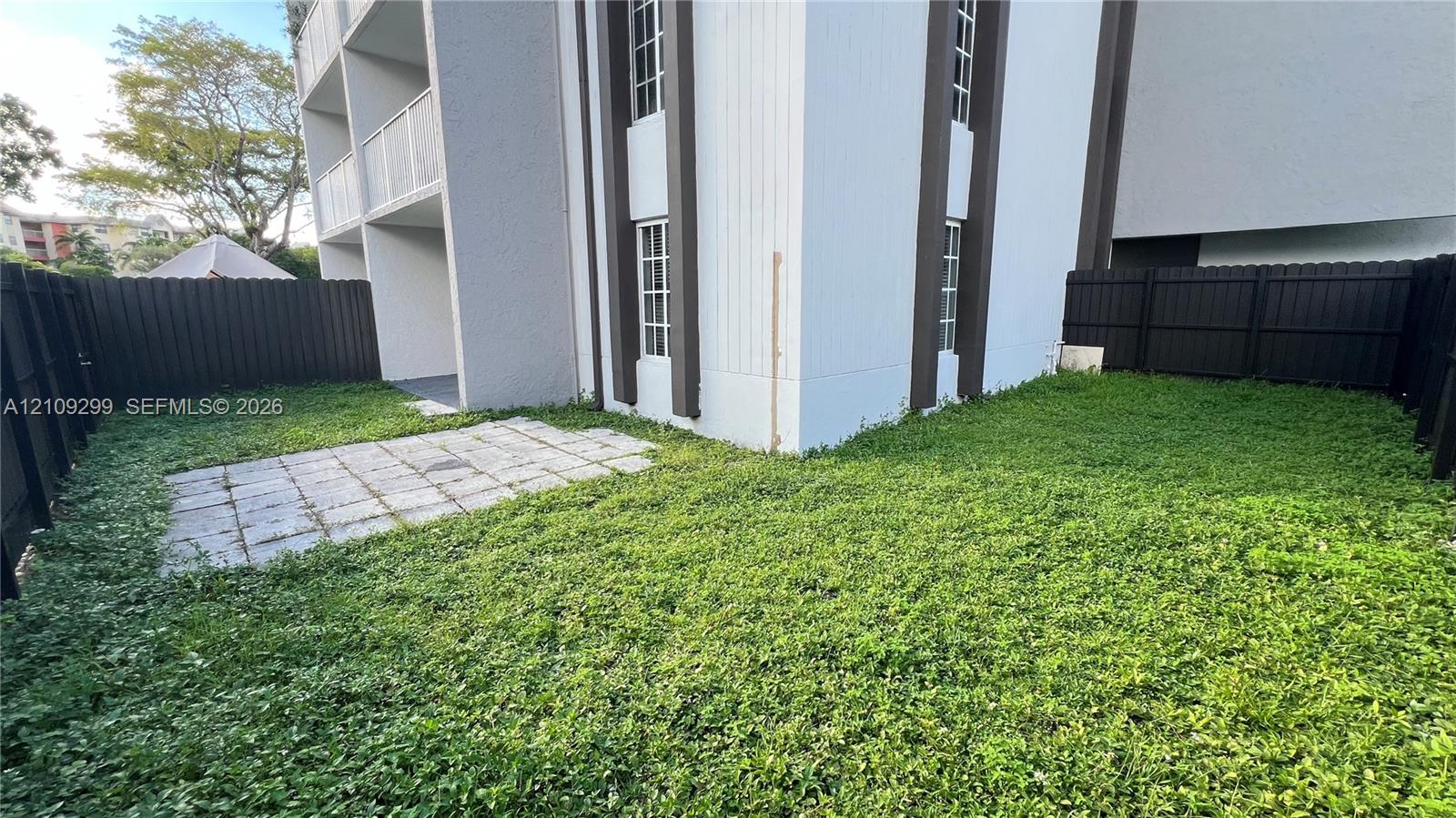 Private rear yard featuring a paved patio, perimeter privacy fencing, and exterior multi-story structure with grid-pane windows