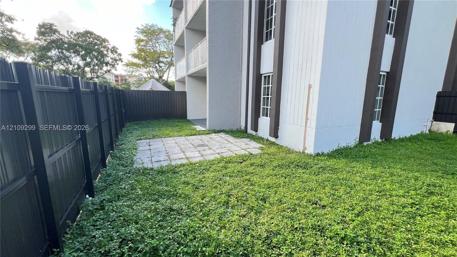 Ground-level patio space enclosed by a black metal privacy fence, featuring exterior siding with vertical trim accents and multi-pane windows
