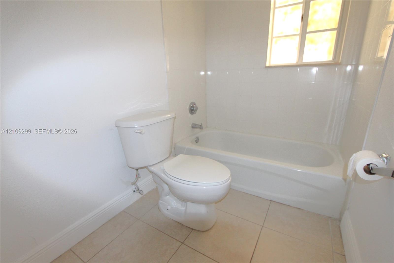 Full bathroom featuring a white porcelain toilet, integrated bathtub and shower combination with tile surround, and neutral-toned floor tile