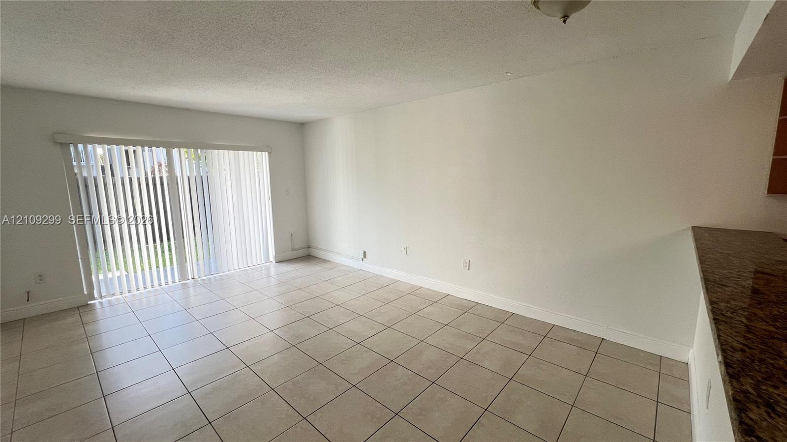 Interior space featuring light-toned ceramic tile flooring, sliding glass door with vertical blinds, and stone-finish countertop