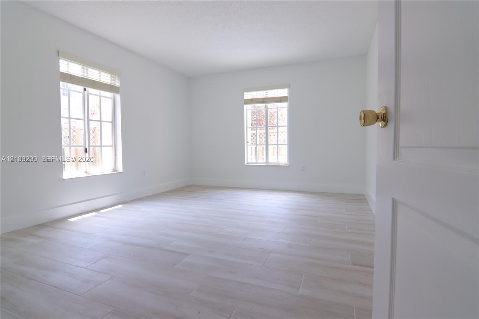 Neutral-toned wood-finish flooring, two multi-pane windows with integrated blinds, and a solid-core interior door with polished brass hardware