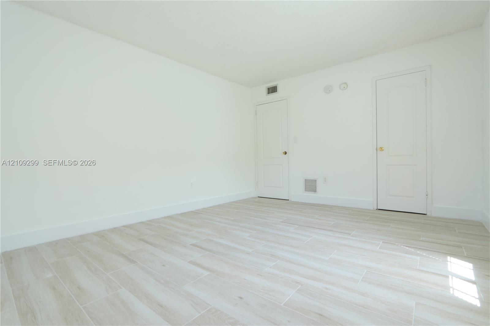 Interior space featuring neutral wall paint, wood-finish tile flooring, and two interior doors with brass hardware