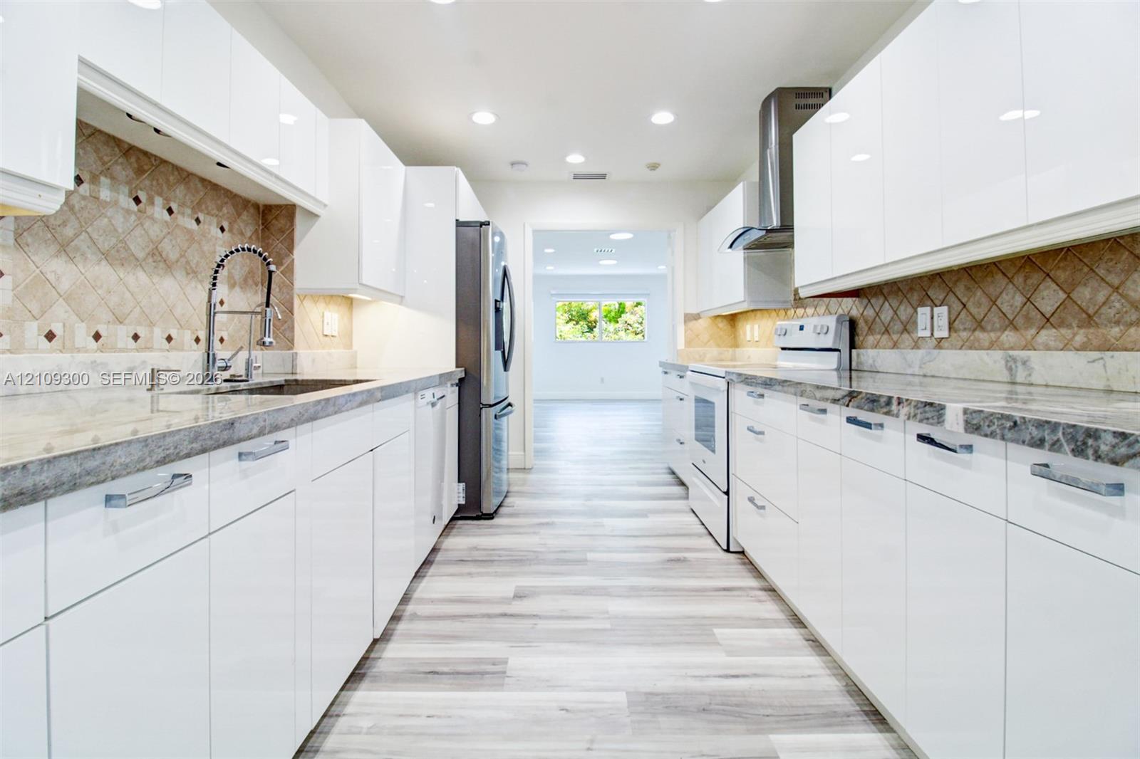 Kitchen featuring high-gloss white cabinetry, stone countertops, stainless steel appliances, a diagonal-patterned tile backsplash, and wood-finish flooring