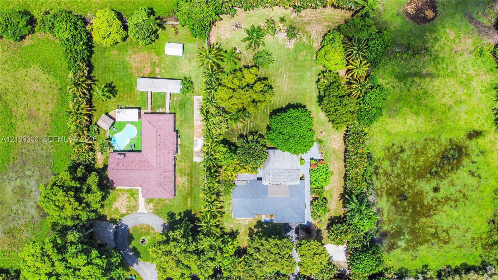 Aerial perspective of a sprawling property featuring two distinct residential structures, a swimming pool, mature perimeter landscaping, and expansive acreage