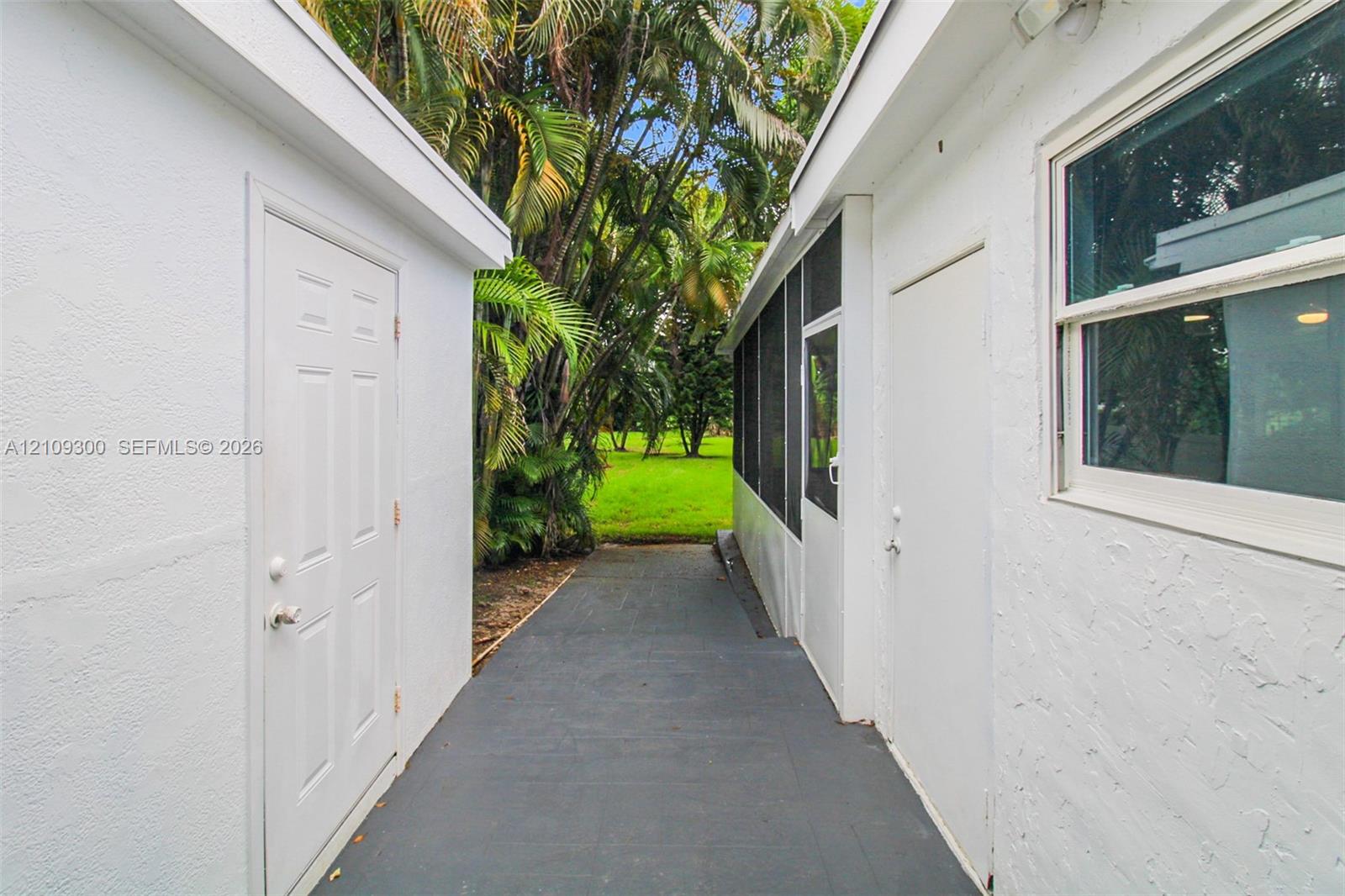 Stucco exterior walls, gray painted concrete pathway, screen-enclosed area, and mature landscape