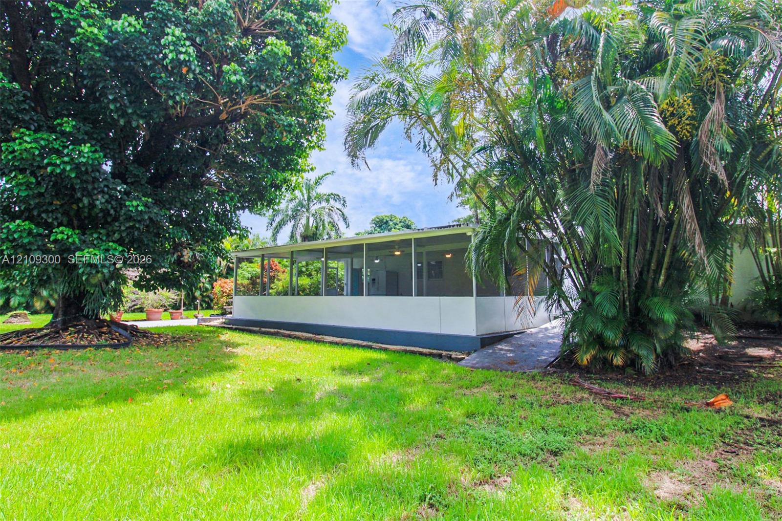 Screen-enclosed porch featuring a concrete foundation, integrated ceiling fans, and a paved walkway, situated on a lawn with mature trees