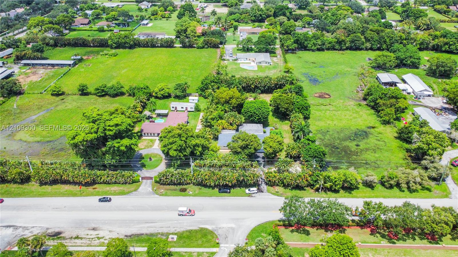 Aerial perspective of expansive acreage featuring mature trees, manicured landscaping, a circular driveway, and a gated entrance