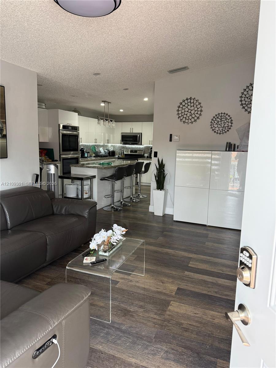 Kitchen featuring white flat-panel cabinetry, stone-finish countertops, built-in wall oven, and recessed lighting, with wood-finish flooring throughout