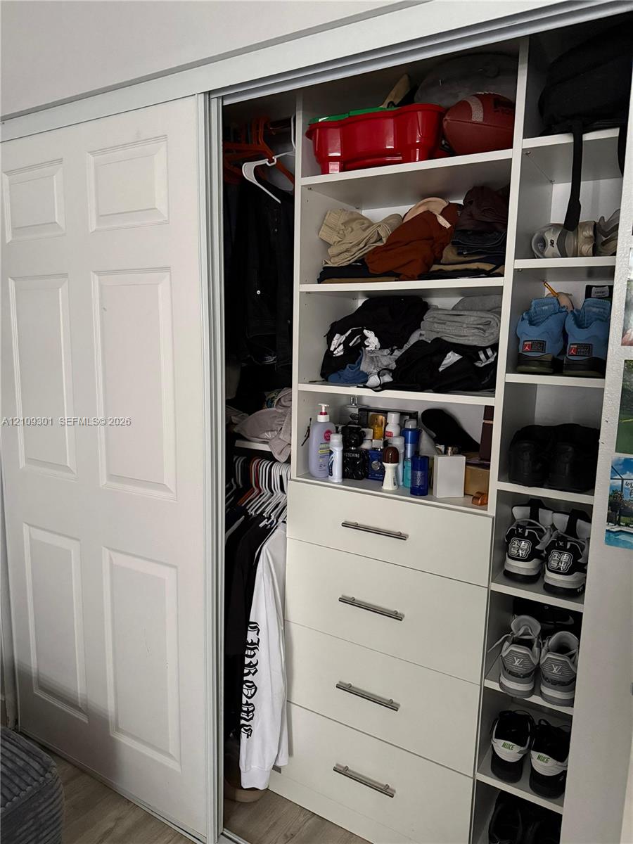 Closet featuring sliding six-panel doors, integrated white shelving, built-in drawer stack with metallic pulls, and dedicated vertical shoe storage