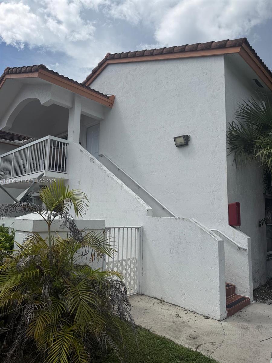 Stucco exterior featuring a tiled roof, upper-level balcony with metal railing, and concrete staircase with integrated handrail
