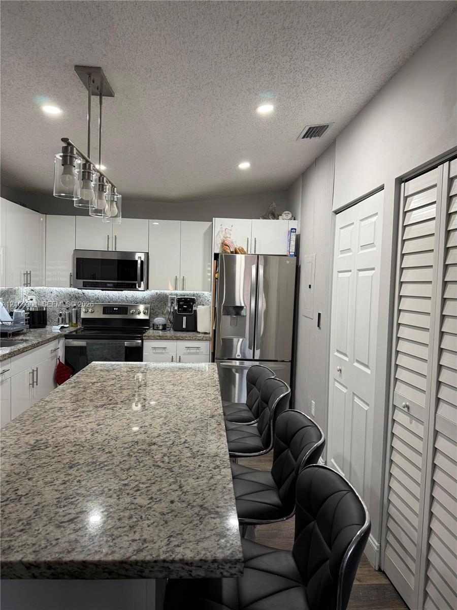Kitchen featuring a large central island with stone countertop, gloss-finish cabinetry, stainless steel appliances, and a multi-light pendant fixture