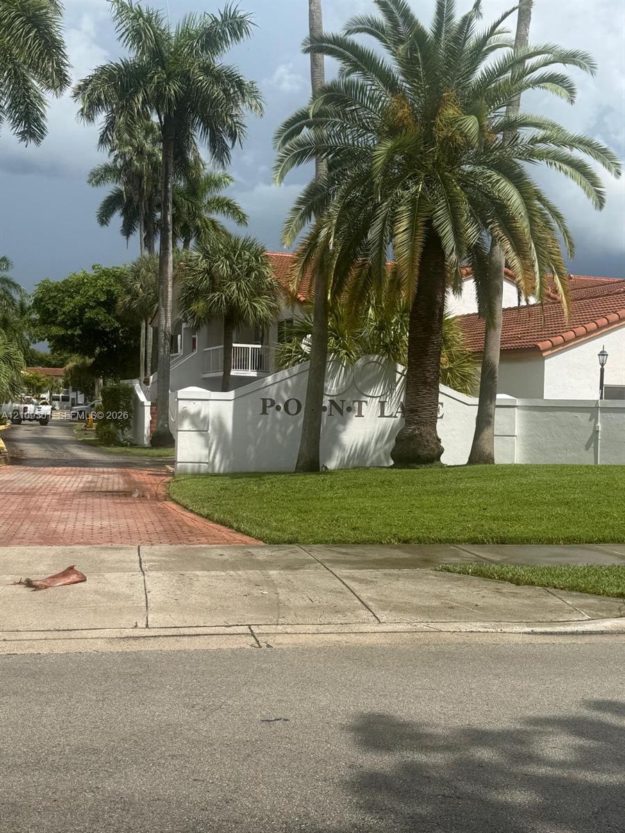 Stucco monument signage featuring mature palm trees, tile roof structures, and paved brick driveway