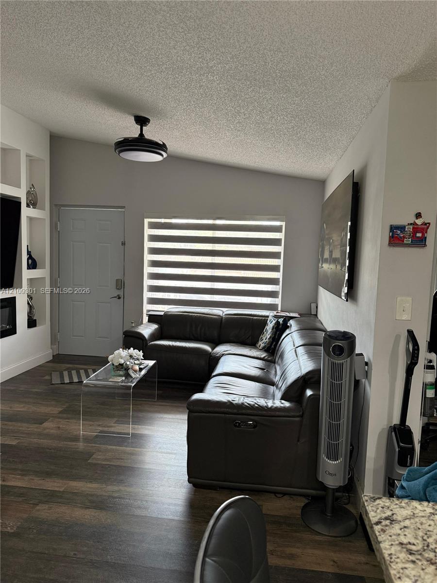 Living area featuring wood-finish flooring, vaulted ceilings, built-in shelving, and a modern ceiling fan with integrated lighting