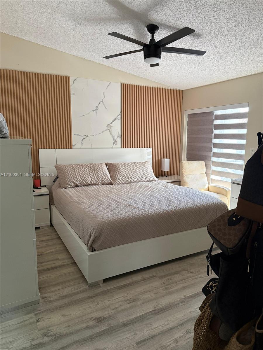 Accent wall featuring vertical slatted panels and a central stone-patterned tile inlay, wood-finish flooring, and a ceiling-mounted fan with integrated lighting