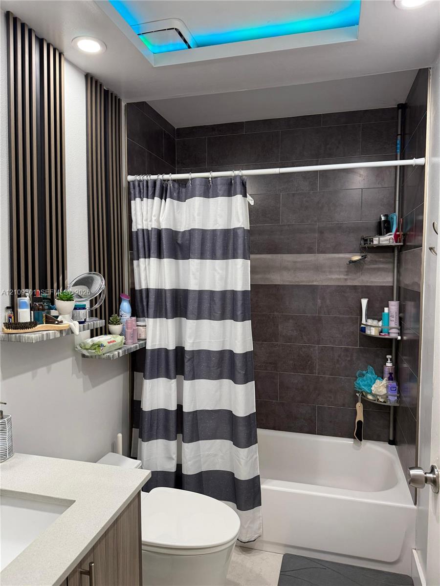Bathroom featuring large-format dark charcoal tile shower surround, integrated LED ceiling lighting, vertical slat wall accents, and vanity with solid-surface countertop
