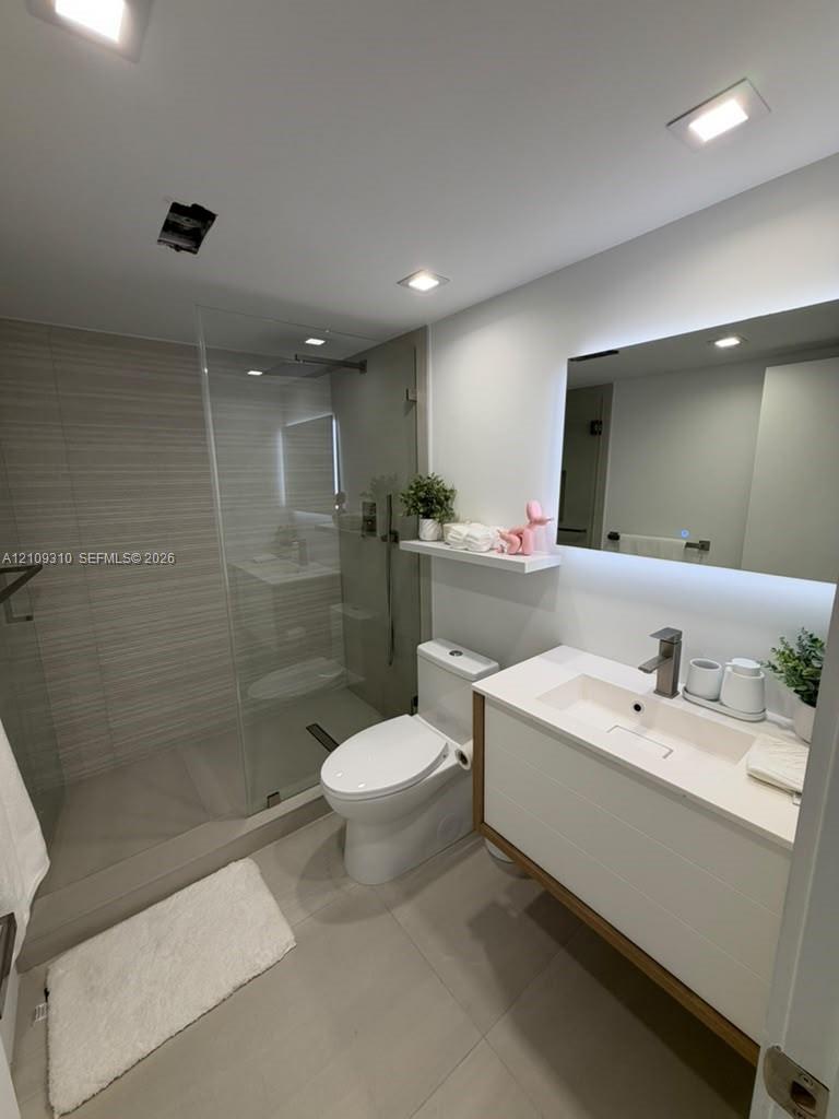 Walk-in shower with horizontal tile surround and glass partition, floating vanity featuring a rectangular integrated sink, white countertop, and LED-backlit mirror