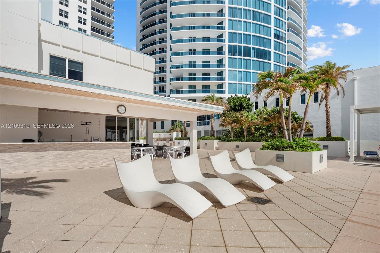 Outdoor terrace featuring a covered bar area with stone-tile facade, concrete pavers, and integrated palm tree planters